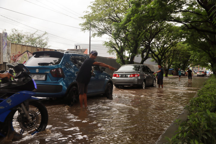 Pak ogah mengarahkan pengendara motor untuk melintasi jalanan yang tergenang air